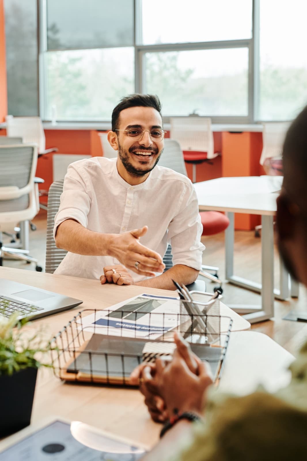 Homem sorridente estendendo a mão para um aperto de mãos em uma mesa de escritório
